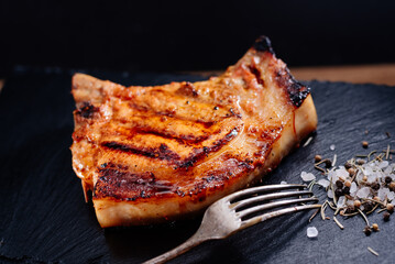 Pork steak on a rib lies on a slate board, next to rice with vegetables, coarse salt with spices