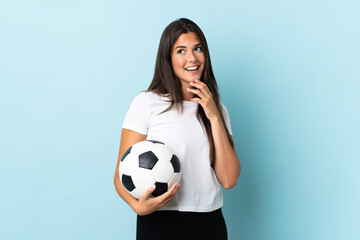 Young football player brazilian girl isolated on blue background looking up while smiling