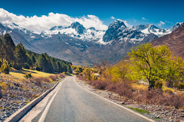 Sunny morning scene of Theth National Park with snowy peaks on background. Picturesque spring view of Albania with asphalt road. Traveling concept background..