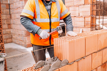 house construction site, worker building the brick wall with trowel, cement and mortar. Professional construction worker working