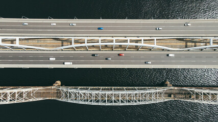 Aerial top view of cars and train passing the bridge over the river in the city