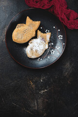 Black plate with japanese traditional taiyaki cakes over dark-brown stone background, vertical shot with space, top view