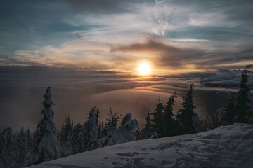 Dramatic Sunset with Trees and Low Clouds View Landscape from Mountain Peak with deep snow