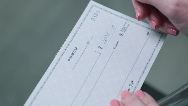 business woman hand signs and filling bank check for one thousand 1000 dollars