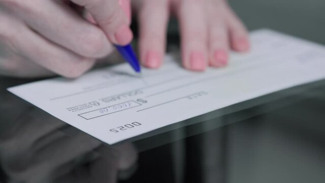 business woman hand signs and filling bank check for one thousand 1000 dollars