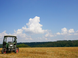 Old green small tractor on a grain field in the nature in summer with sunshine.