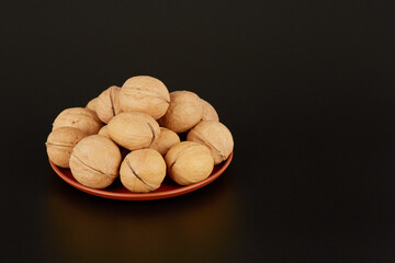 Many walnuts lie on a clay plate on a black background