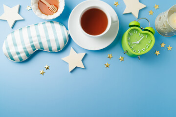 Healthy sleeping concept with herbal tea, alarm clock and sleeping mask on blue background. Top...
