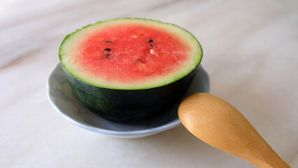 Small round watermelon cut into half, served on a small plate. With a wooden spoon at the side.