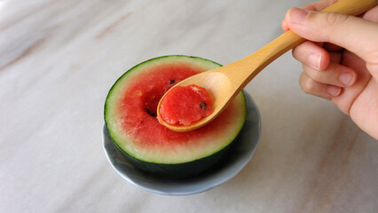 Hand holding a wooden spoon, digging into a small watermelon cut in half.