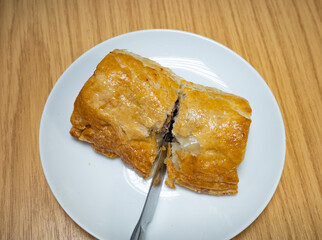 Unidentified person cutting a homemade sausage roll with a stainless steel kitchen knife