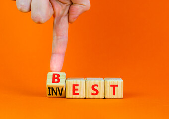 Best invest symbol. Businessman turns a wooden cube and changes the word Invest to Best. Beautiful orange table, orange background. Business and best invest concept. Copy space.