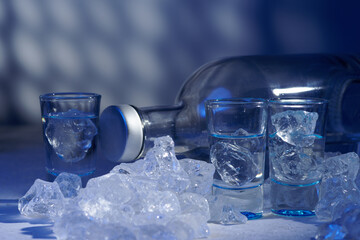 Glass of vodka with ice on blue background, selective focus