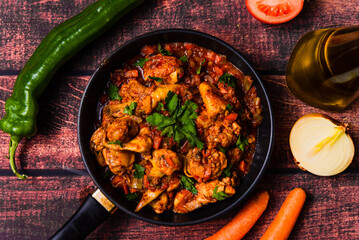 chicken cacciatore dish in a pan close up. traditional dish of italian cuisine with parsley, bell pepper, tomato, olive oil and onions on wooden kitchen table