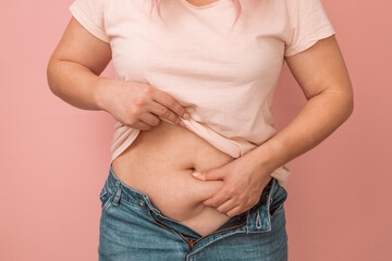 Woman hand holding excessive belly fat, overweight concept. Overweight female wearing a jeans