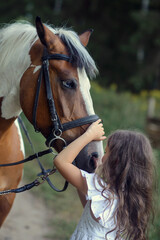 Fototapeta premium little caucasian girl with a horse at the horse farm in the forest in summer
