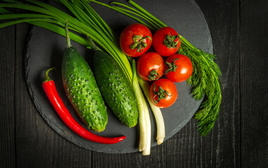 Fresh vegetable salad set. Red tomatoes and green young onions with cucumber on a black plate. Vitamin breakfast or dinner