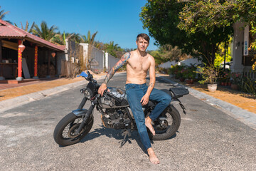 Fototapeta premium Young shirtless caucasian man with full-arm tattoo sitting on motorcycle