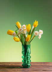 spring flowers in green glass vase on wooden table