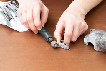 Manos con una lijadora, lijando una pieza rota de metal para unirla con adhesivo
