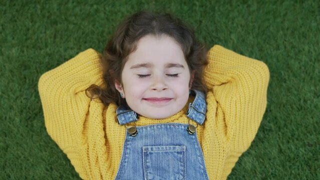 Happy girl with closed eyes stretched out on artificial turf enjoying good weather spring summer. Imitation grass for gardens and outdoor spaces