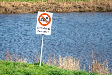 Fototapeten Sign reading "Forbidden to swim" (Dutch: verboden te zwemmen) near a river © Menyhert