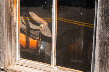 A saddle on a drum barrel inside a barn through a window.