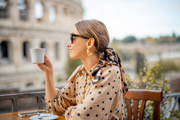 Woman drinking coffee at outdoor cafe near coliseum, the most famous landmark in Rome. Concept of italian lifestyle and traveling Italy. Caucasian woman wearing dress and shawl in hair