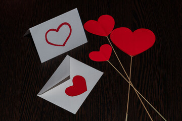 Three cardboard hearts on the rays of sticks intersect at one point. A love letter with a red heart and an envelope with a heart seal, surrounded by hearts, for Valentine's Day.