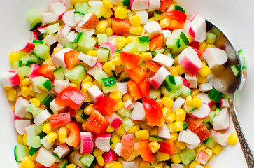 salad of cucumbers, corn, bell peppers and crab sticks in a white bowl. Close-up.