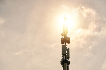 Telecommunication tower of 5G cellular. LTE radio network communication equipment with wireless modules and smart antennas mounted on metal pillar on clouds and sun sky background.