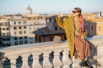 Woman enjoying beautiful morning cityscape of Rome, taking photo on phone, while sitting on the top of famous Spanish steps. Concept of italian lifestyle and travel