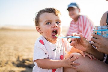 Mother feeding a baby on a beach during sunset