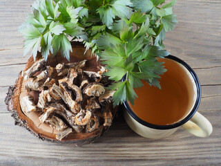 Root, herbal drink in a mug and spicy herb lovage with green leaves in a wooden spoon. Medicinal...