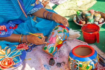 Rural Indian woman in traditional costume painting a clay vase for sale at handicraft fair at...