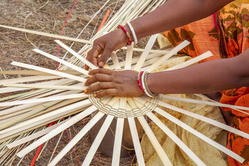 Hands of a rural Indian woman in closeup weaving a basket with bamboo straws
