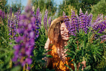 Portrait of young woman holding bouquet of lupin flowers walking in summer meadow. Stylish girl...