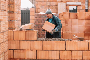 professional construction worker laying bricks and building walls at industrial site. Detail of...