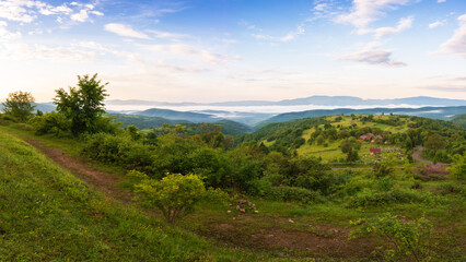 Fototapeta na wymiar carpathian rural landscape in spring at sunrise. trees on the grassy hills rolling in to the distant valley in morning light. fluffy cloud formations on the sky. beautiful nature background