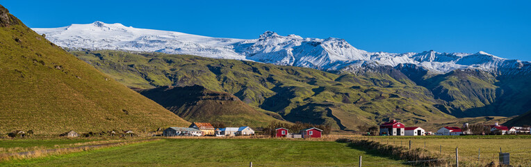 Fototapeta na wymiar View from highway road during auto trip in Iceland. Spectacular Icelandic landscape with scenic nature: hamlets, mountains, ocean coast, fjords, fields, clouds, glaciers, waterfalls.