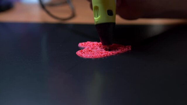 A girl draws a heart with a 3D pen. The daughter creates a beautiful pink keychain as a gift for mom on mother's day or for dad on father's day. close-up work 3d pens.