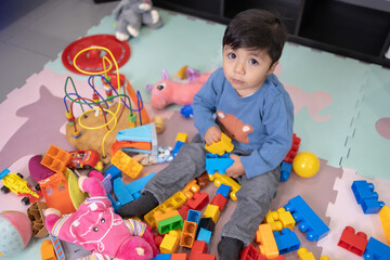 two years old mexican baby boy playing with didactic toy on messy living room