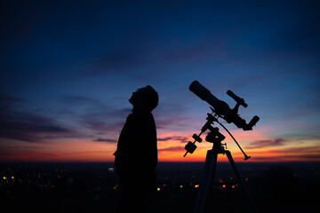 Silhouette of a man, telescope and countryside under the starry