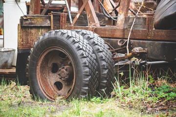 Fototapeta na wymiar double wheel of old abandoned no more used car, rusty metal parts, growing in grass