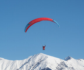 Naklejka na ściany i meble People in tandem paragliding over winter snowy mountains at clear blue sky background