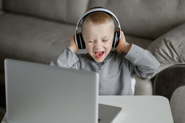 The boy at the PC,listens to music and sings,holding headphones with his hands.