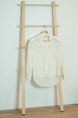 Classic white silk women blouse hanging on wooden hanger ladder.