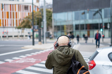 Rear view of an unknown man with white hair crossing the street listening to music with headphones