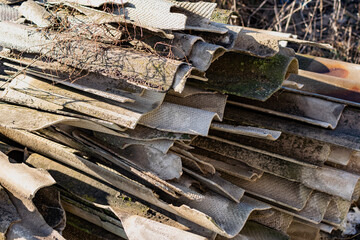 Broken pieces of slate, taken from the roof, are collected in a large high stack in the garden among dry grass, in the warm sun, a pile of building materials