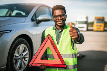 Young African American man putting safety or warning foldable triangle on the road. Help on the...